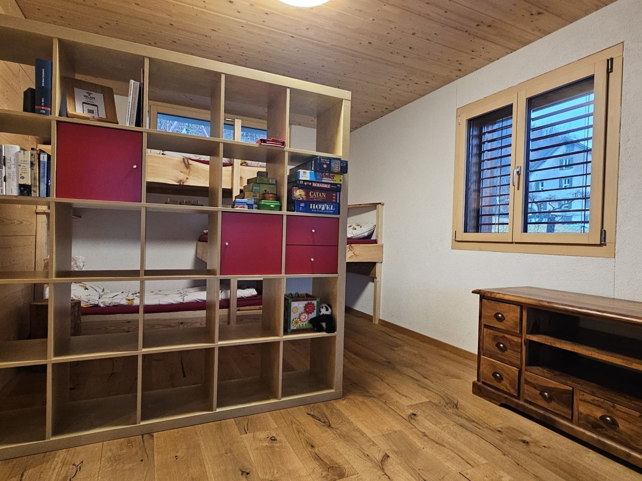 Une pièce avec une bibliothèque en bois, une fenêtre avec des stores et un petit bureau en bois.