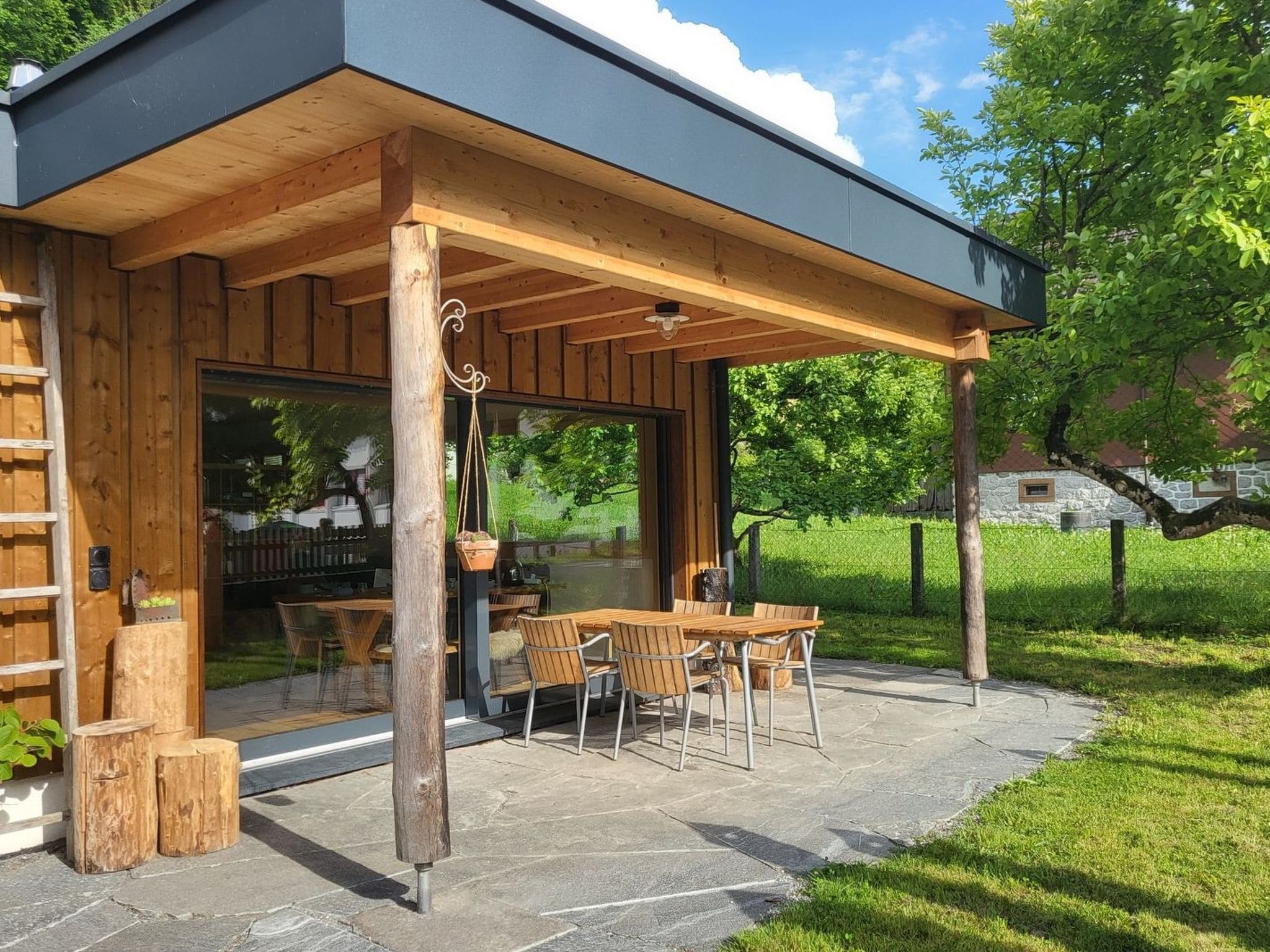 A wooden outdoor patio with tables and chairs, a covered seating area, and a stone pathway.