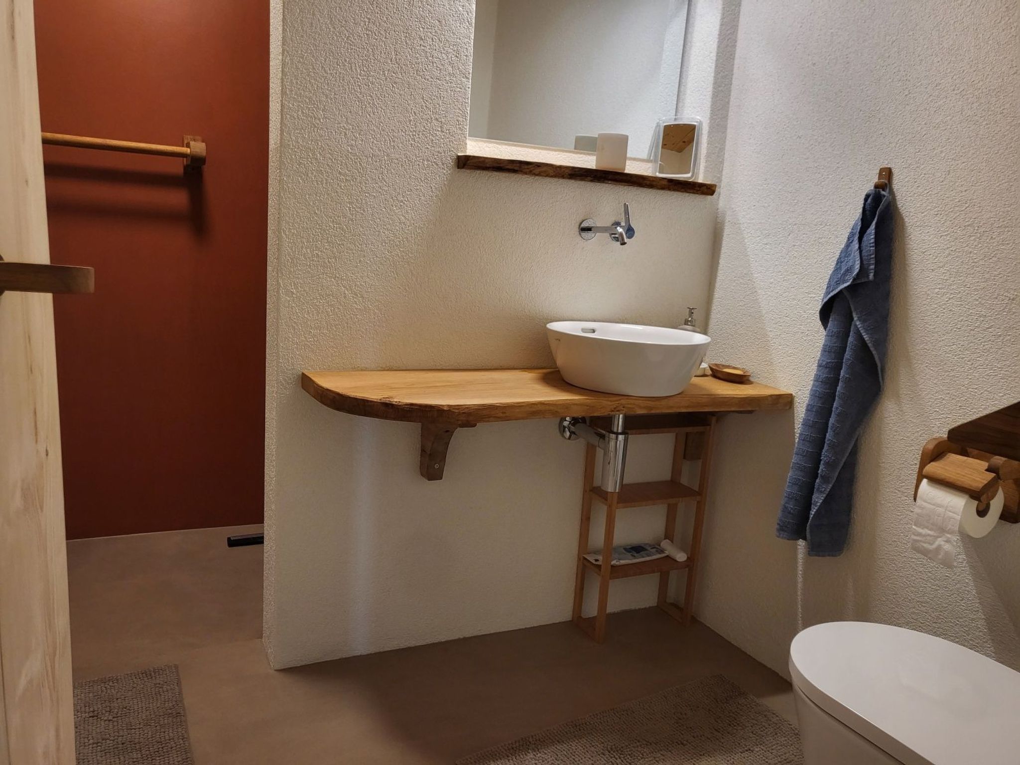A compact bathroom with a wooden vanity, a white sink, a mirror, and a towel rack.