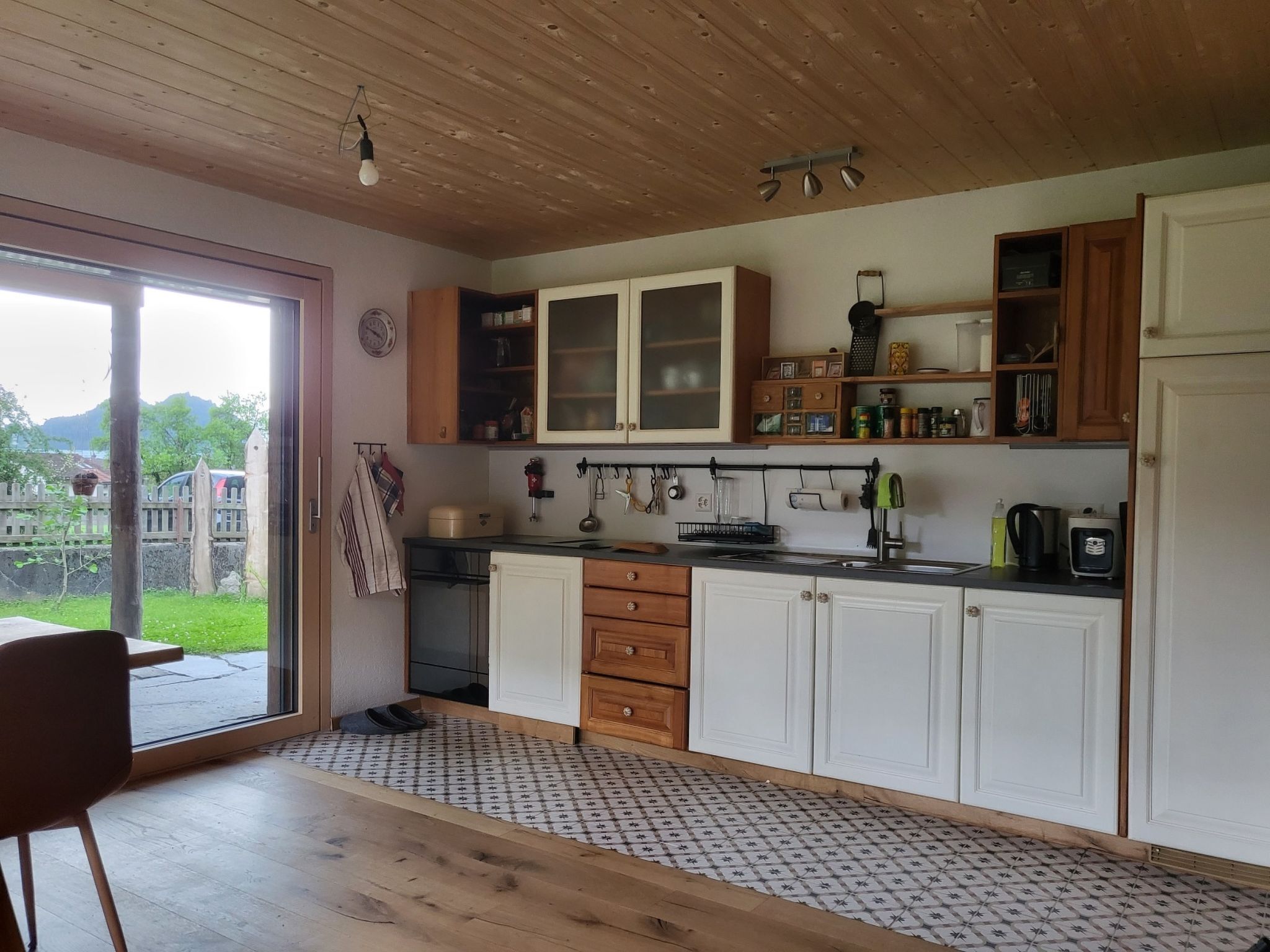 Une cuisine avec des meubles de rangement en bois, un évier et une fenêtre donnant sur un jardin.