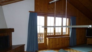 A wooden interior with a dining table, chairs, a television, and a window with curtains.
