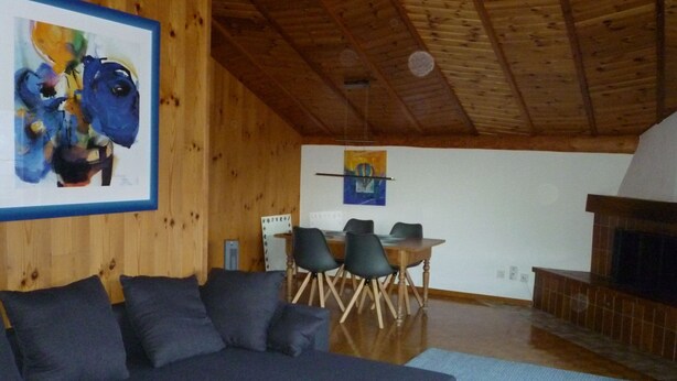 A living room with a sectional sofa, a dining table with chairs, a fireplace, and artwork on the walls.