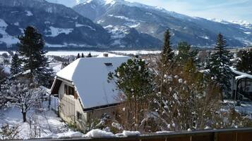 Un paysage de montagne enneigé, avec une maison au premier plan.
