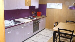 A compact kitchen with purple cabinets, a wooden dining table, and a coffee machine.