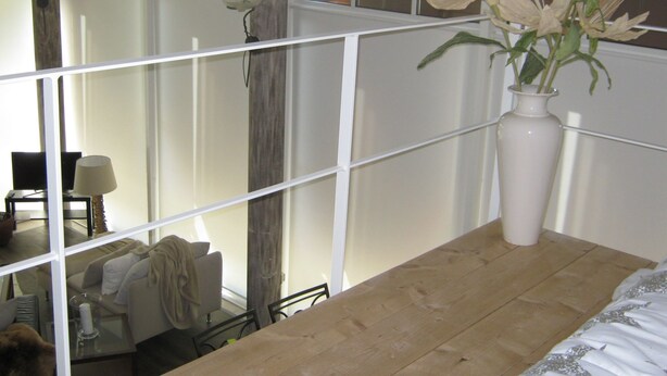 Ein Zimmer mit einem Holztisch, einer weißen Vase mit Blumen, einem Stuhl und einem Sofa.