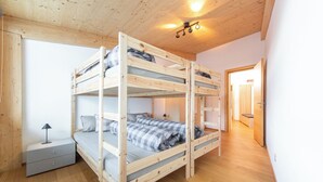 A bunk bed room with a wooden ceiling, a bedside table, and a lamp.