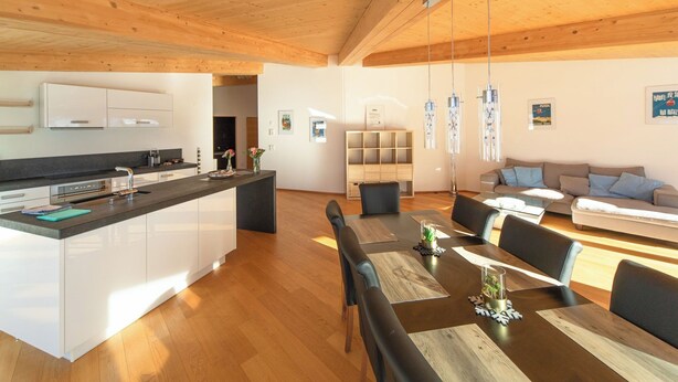 A modern kitchen with white cabinets, a central island, and a dining area with a wooden table and chairs.
