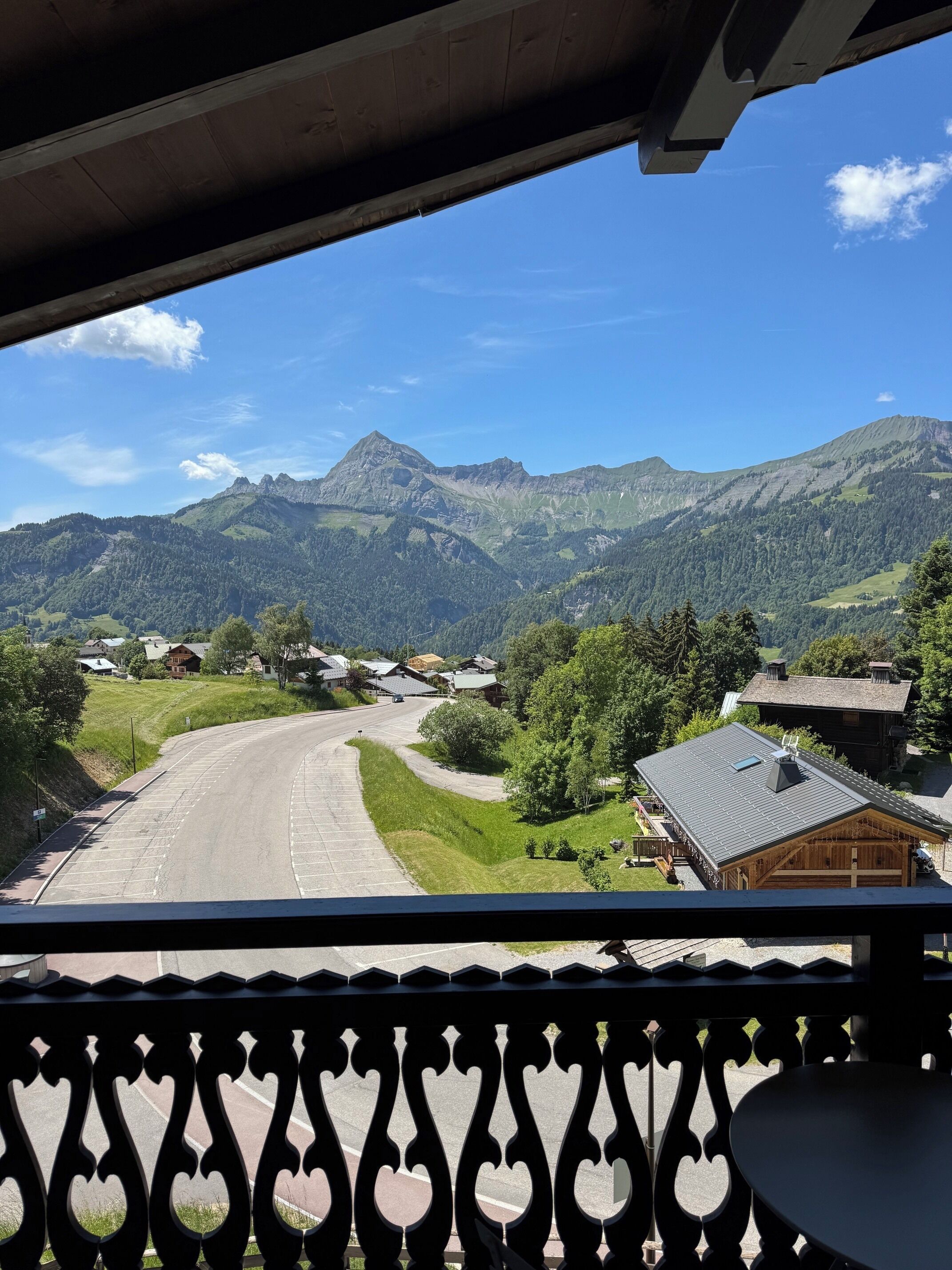 A mountain view from a balcony with a railing, a road, and houses in the valley.