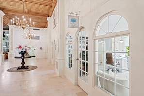 A spacious hallway with a chandelier, a round table with flowers, and arched windows. - The Island Terrace Suite at Palm Beach Hotel (Palm Beach)