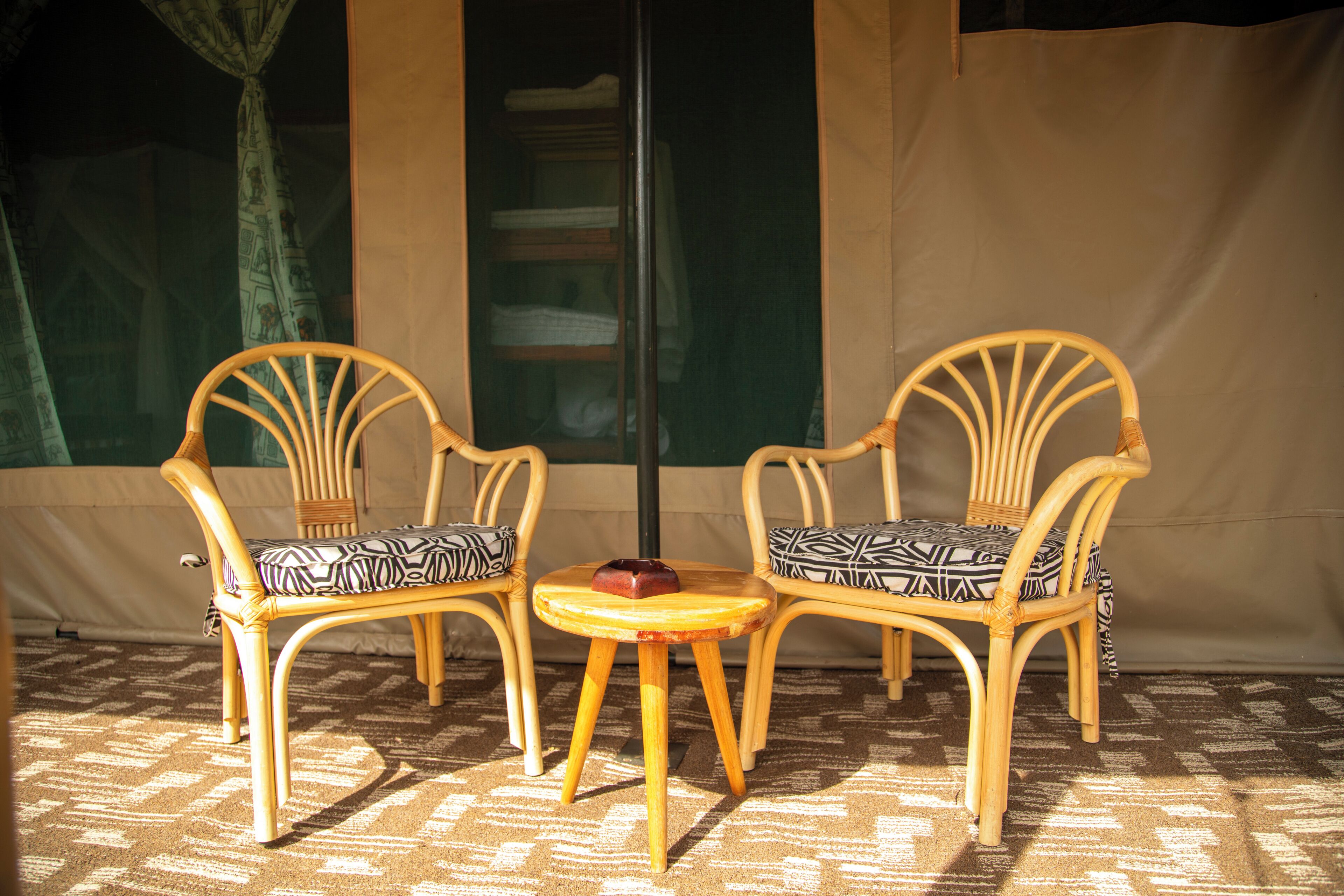 Deux fauteuils en osier avec des coussins à motifs, une petite table en bois ornée d’un objet décoratif et un tapis à motifs.