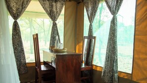 A room with a wooden table, two chairs, zebra-patterned curtains, and a view through the window.