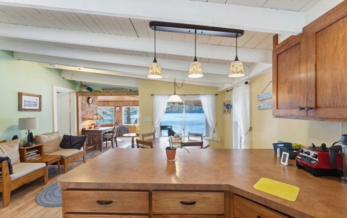 Un vaste espace de vie comprenant un coin repas avec une table en bois, un canapé et une cuisine dotée d’un grand îlot central.
