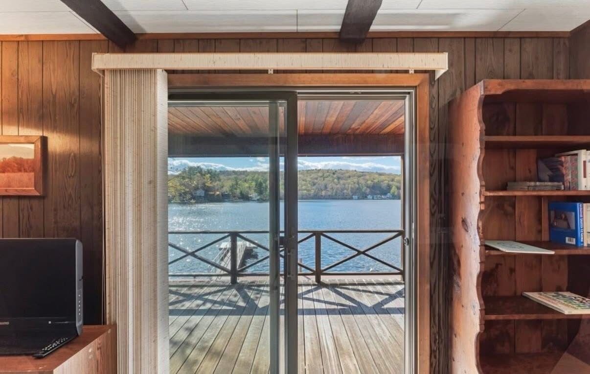 Un intérieur en bois avec une porte-fenêtre coulissante donnant sur une terrasse qui offre une vue sur un lac.