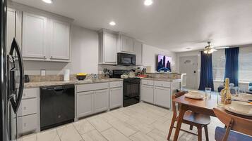 A modern kitchen with white cabinetry, a dishwasher, a microwave, and a dining area with a table and chairs.