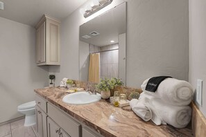 A bathroom with a marble countertop, a white sink, a mirror, and a towel rack with a towel.