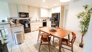 Una cocina moderna con armarios blancos, un refrigerador de acero inoxidable, una mesa de comedor de madera con sillas y una planta en maceta.