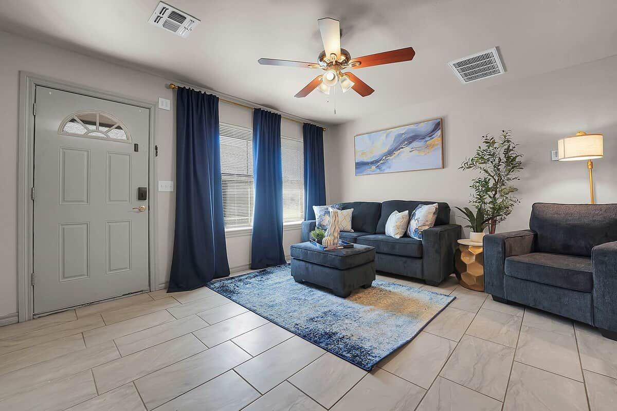 A living room with a ceiling fan, a grey door, a blue rug, and a sofa.