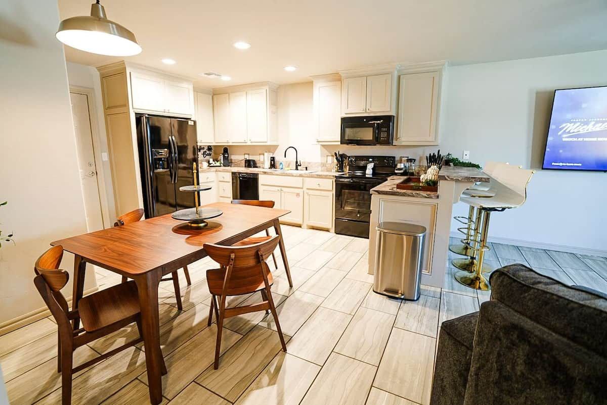 A modern kitchen with a dining table, chairs, a refrigerator, microwave, and a TV.