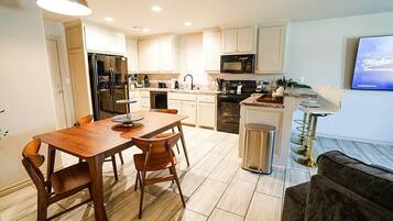 A modern kitchen with a dining table, chairs, a refrigerator, microwave, and a TV.