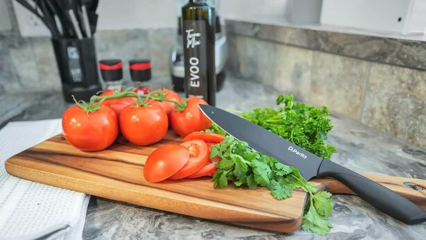 Un plan de travail de cuisine avec une planche à découper, des tomates, un couteau et une bouteille étiquetée « EVOO ».