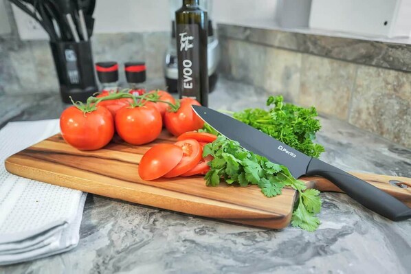 A kitchen counter with a cutting board, tomatoes, a knife, and a bottle labeled 'EVOO'.