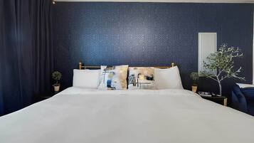 A hotel room with a large bed, dark patterned wallpaper, a potted plant, and a nightstand.