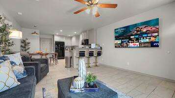A modern living room with a sofa, a coffee table with decorative items, a ceiling fan, and a wall-mounted TV displaying a movie poster.