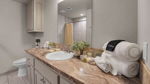 Une salle de bain avec un comptoir en marbre, un lavabo blanc, un miroir et un porte-serviettes avec une serviette.