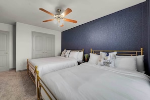 A hotel room with two beds, a ceiling fan, a patterned wall, and a door.
