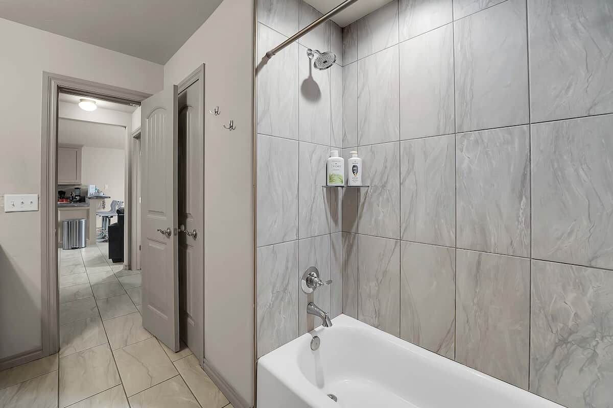 A bathroom with a bathtub, a shower, and a toilet. There are two bottles on a shelf above the bathtub.