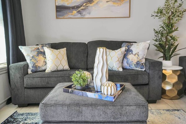 A grey sofa with patterned cushions, a tray with decorative items, and a plant in a white pot.