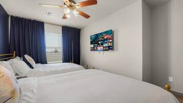 A hotel room with two beds, a ceiling fan, a large window with curtains, and a wall-mounted television.
