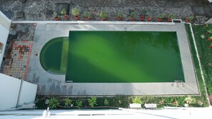 Una piscina en la azotea con un jardín circundante, una pequeña piscina circular y un edificio blanco al fondo.