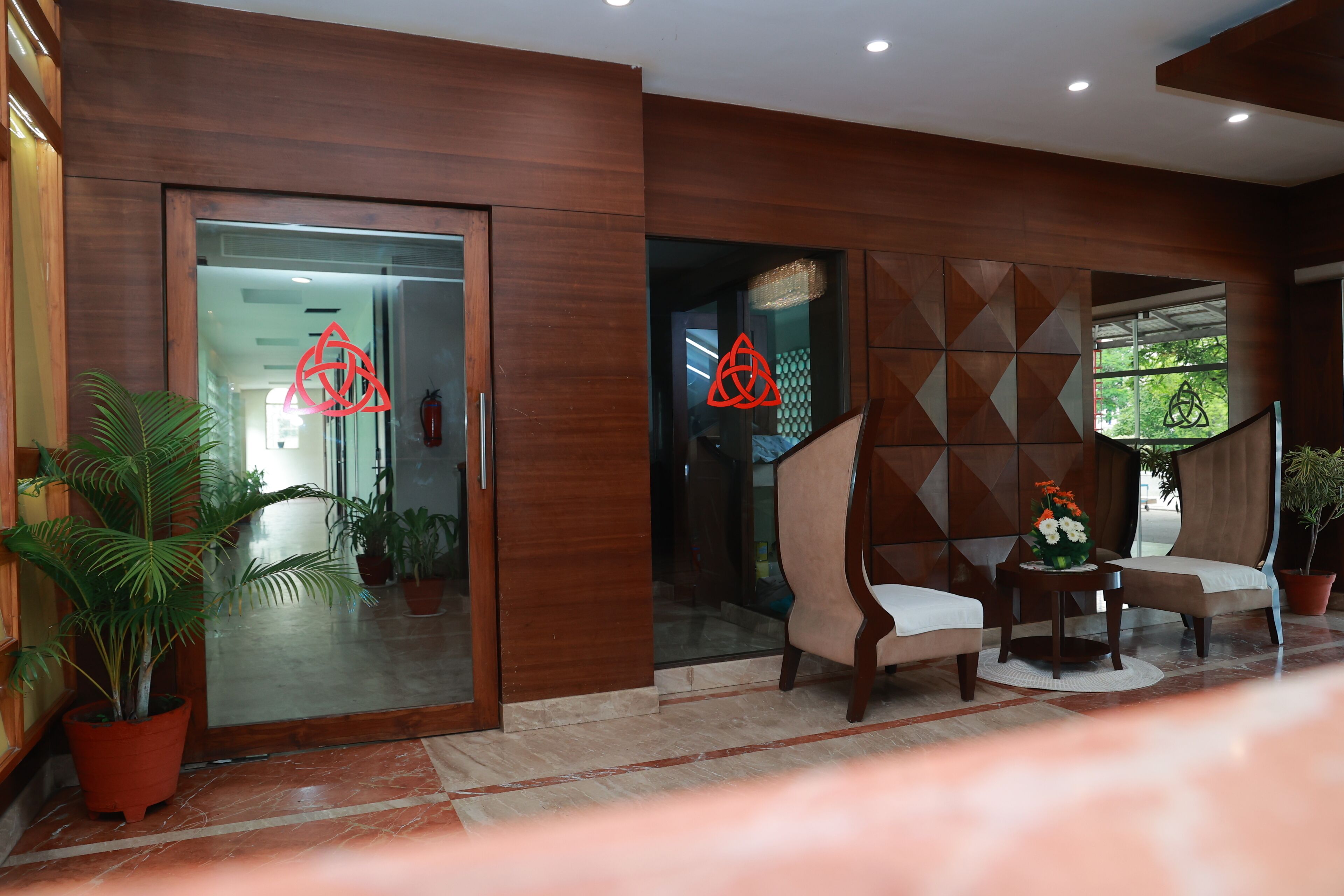 A lobby with wooden paneling, a glass door entrance, potted plants, and a seating area with a small table.