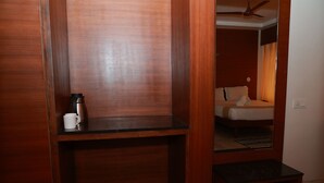 Un escritorio de madera con una cafetera y una taza, una cama con almohadas y un ventilador de techo en una habitación de hotel.