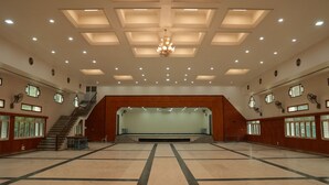 Un hallo espacioso con un escenario central, una escalera y varias ventanas.