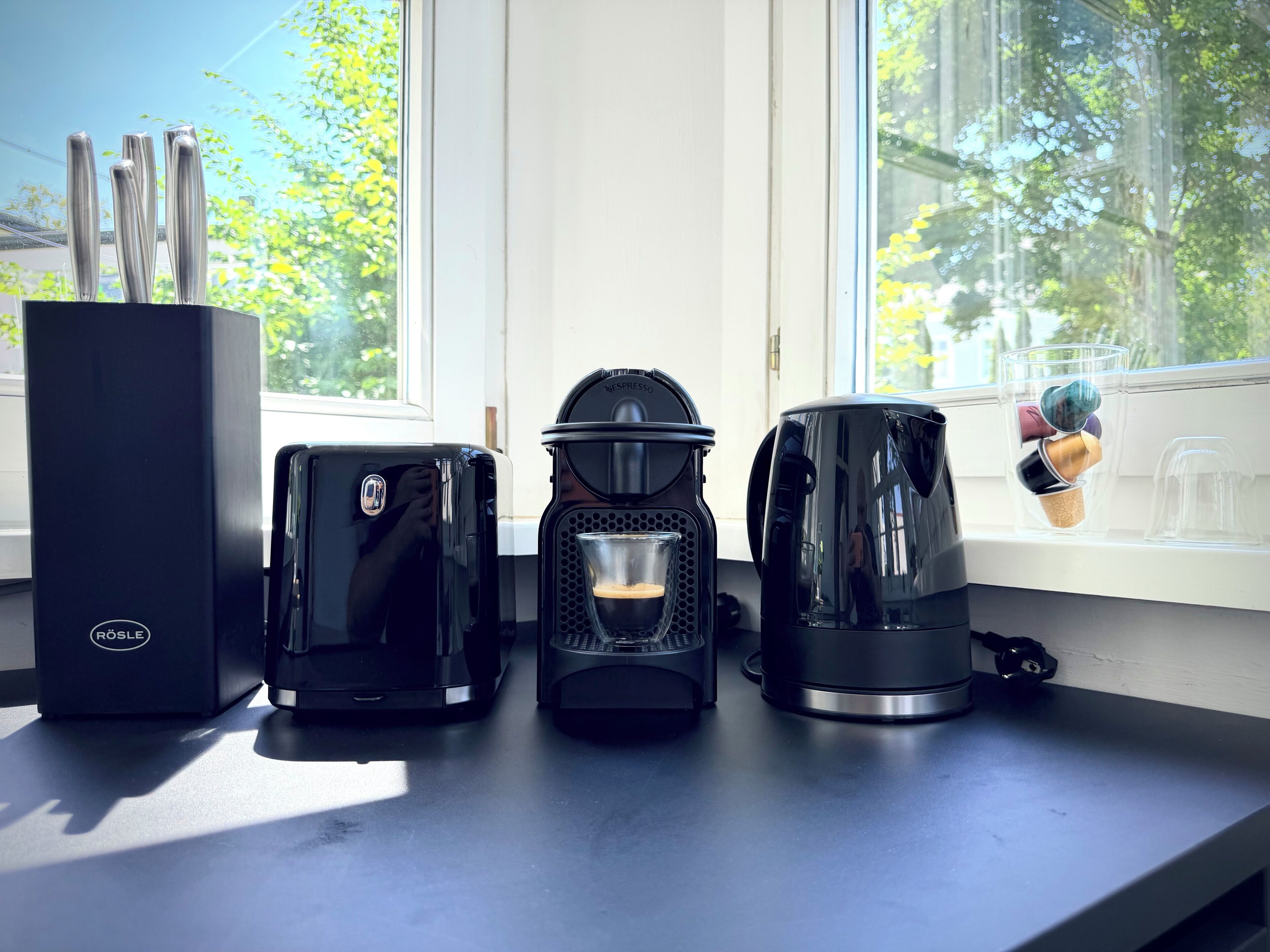 A coffee maker, a Nespresso machine, and a coffee cup on a windowsill.