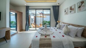 Habitación de hotel con cama, escritorio, silla, balcón con vistas y luz en el techo.