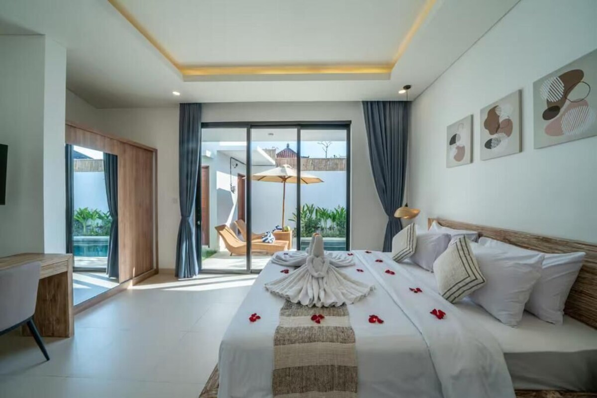 A hotel room with a bed, a desk, a chair, a balcony with a view, and a ceiling light.