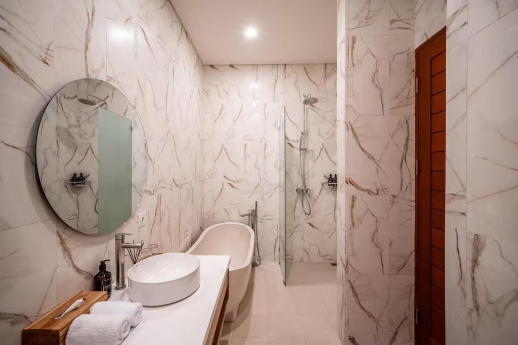 Une salle de bain moderne avec une baignoire sur pieds, une douche à parois de verre et un miroir rond.