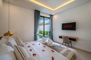 A modern hotel room with a bed, a desk, a TV, and a view of a pool. - Villa Bagus Seminyak (Badung)