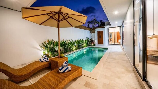 Un área de piscina moderna al aire libre con una silla de descanso, sombrilla y plantas en macetas.