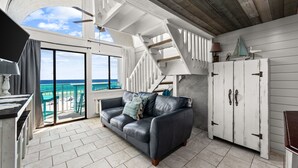 Ein Zimmer mit Ledersofa, einer Treppe, Blick auf den Ozean und einem weißen Schrank.