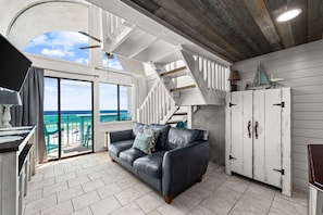 Ein Zimmer mit Ledersofa, einer Treppe, Blick auf den Ozean und einem weißen Schrank.