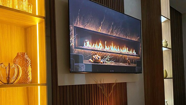 A flat-screen TV mounted on a wall with wooden paneling, a shelf with wine glasses, and a decorative vase. - Cozy luxury apartment in the heart of downtown (agadir)