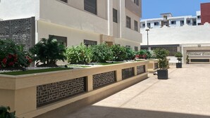 A multi-story building with balconies, a covered parking area, and a landscaped garden with various plants. - Cozy luxury apartment in the heart of downtown (agadir)