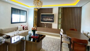 A modern living room with a sofa, coffee table, TV, and dining area. - Cozy luxury apartment in the heart of downtown (agadir)