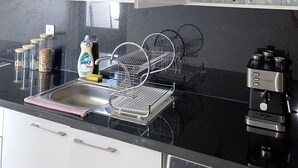 A kitchen with a black countertop, a coffee machine, a dish rack, and open cabinets with dishes and cups. - Cozy luxury apartment in the heart of downtown (agadir)