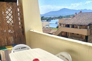 A balcony with a view of a river and buildings, a table with chairs, and a woven partition. - P.Rotondo1 A307 S SEA VIEW (Porto Rotondo)