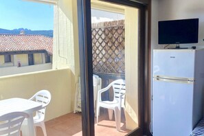 A balcony with a white table and chairs, a white refrigerator, and a television on a stand. - P. Rotondo1 A307 S SEA VIEW (Porto Rotondo)